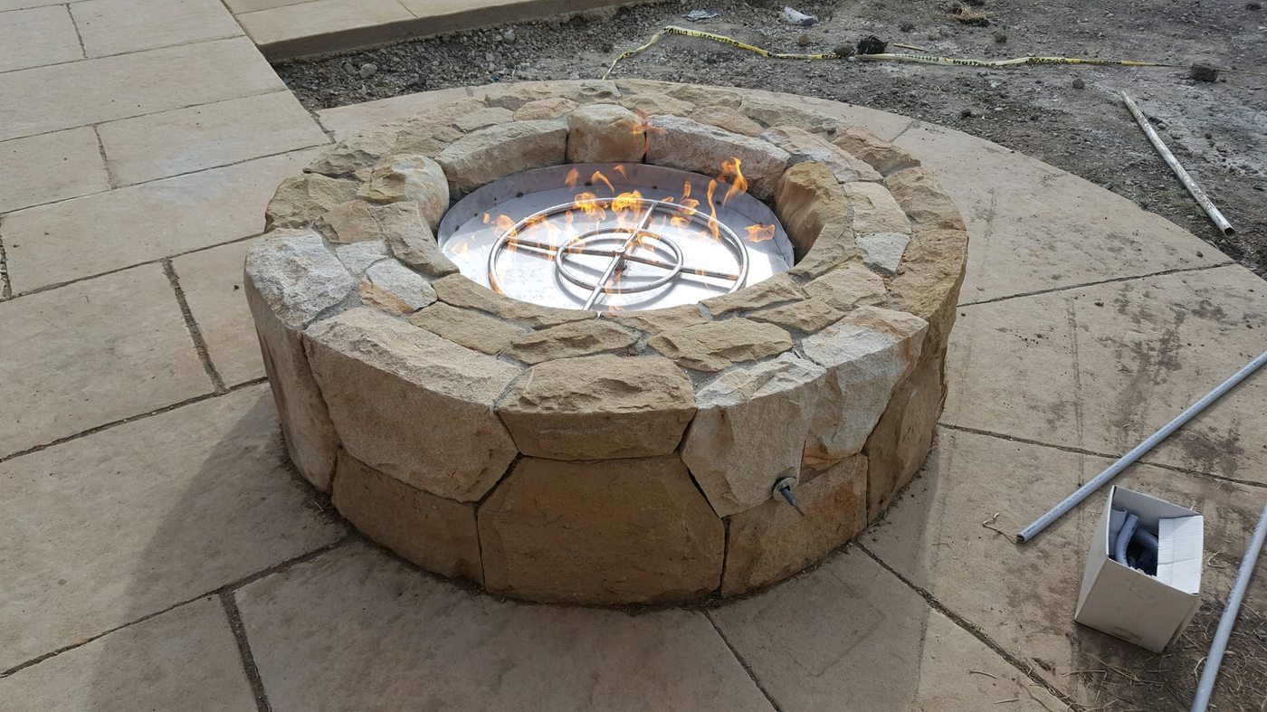 A round stone fire pit with a gas burner ring lit, on a new stone patio.