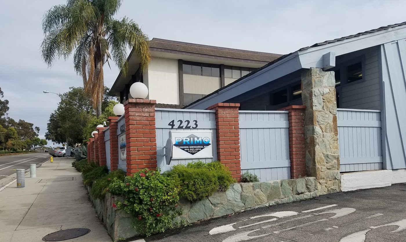 The Primo Plumbing office at 4223 State Street: a sign with the Primo diamond logo on a brick and stone wall, with palm trees along the street.