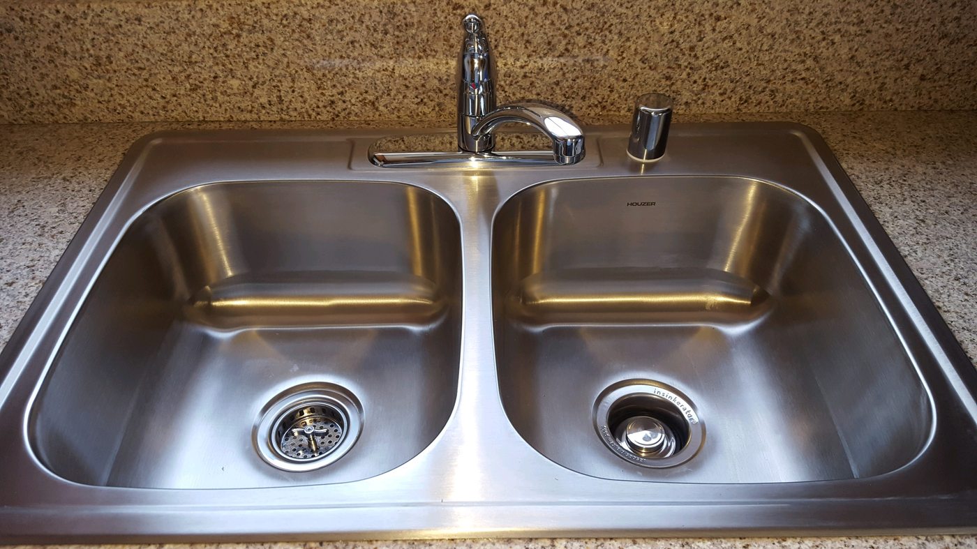 A new stainless double sink and faucet set into a speckled granite counter.